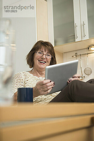 Ältere Frau benutzt ein digitales Tablet und lächelt in der Küche  München  Bayern  Deutschland