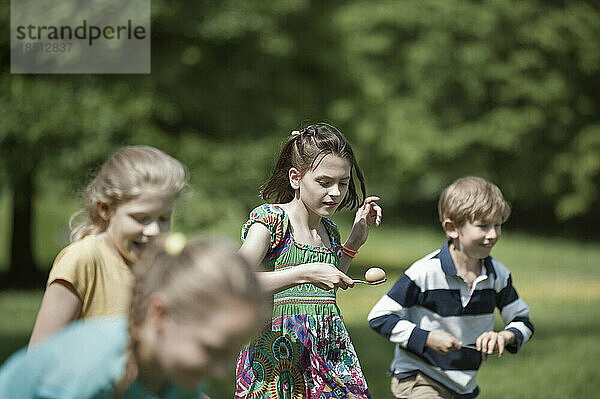 Gruppe von Kindern  die in einem Eier-und-Löffel-Rennen in einem Park in München  Bayern  Deutschland  gegeneinander antreten