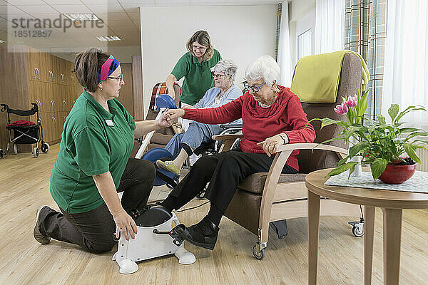Krankenschwester und ältere Frau im Rollstuhl trainieren auf Heimtrainer im Pflegeheim