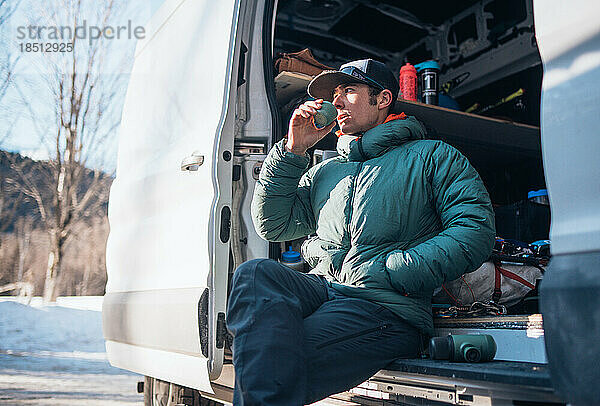 Mann trinkt aus einer Tasse  während er in seinem Wohnmobil sitzt