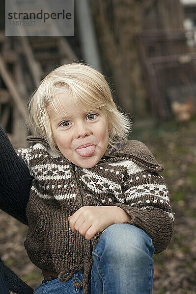 Kleiner Junge streckt seine Zunge auf einem Bauernhof in Bayern heraus