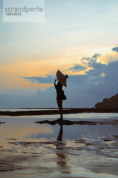 Junge Frau mit großem Strohhut auf dem Meer bei Sonnenuntergang.