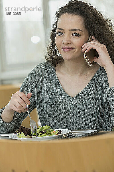 Student isst in der Kantine Salat und telefoniert mit dem Handy. Schule  Bayern  Deutschland