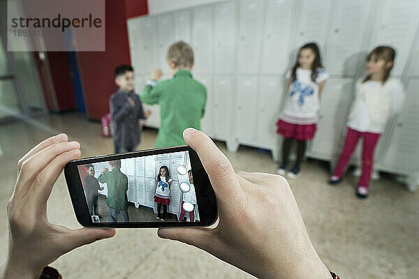 Die Hand einer Person filmt zwei Schüler  die sich im Schulkorridor mit einem Mobiltelefon streiten  Bayern  Deutschland