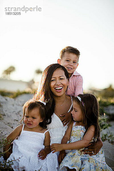 Mutter sitzt mit ihren drei kleinen Kindern am Strand in San Diego