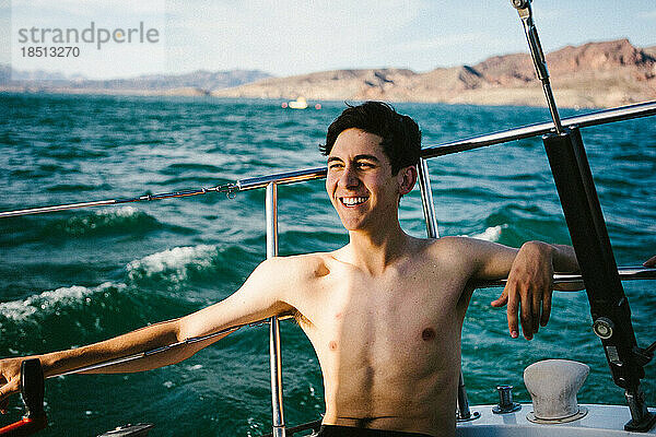 Junger Mann lächelt auf einem Segelboot auf dem See im Sommersonnenschein