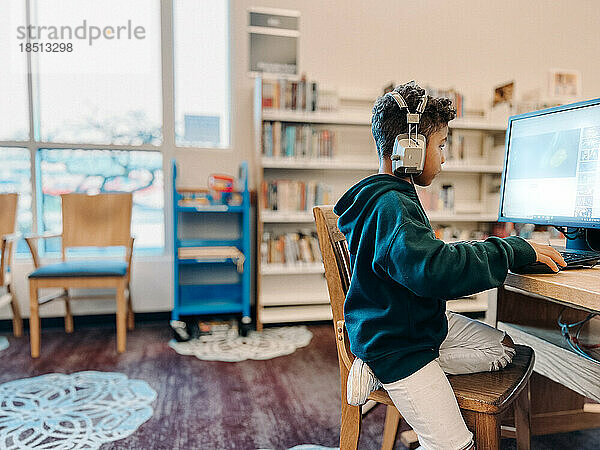 Mischlingsjunge benutzt Computer mit Bücherregalen im Hintergrund