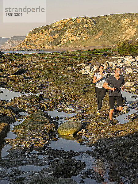 Mann und Frau laufen auf einem Singletrail am Strand von Azkorri