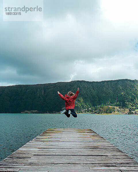Junge Frau springt auf den Steg eines Sees auf den Azoren