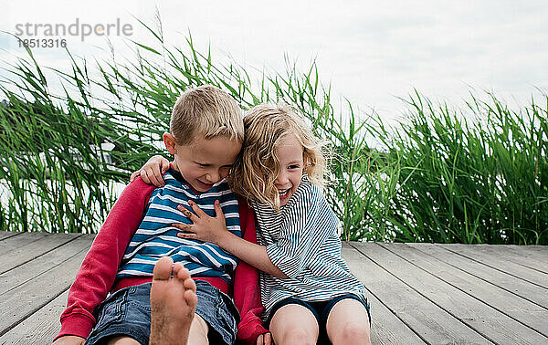 Bruder und Schwester lachen und umarmen sich im Sommer am Strand