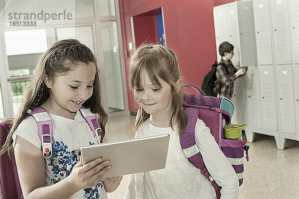 Zwei Schulmädchen schauen auf ein digitales Tablet im Flur in der Nähe von Schließfächern  Bayern  Deutschland