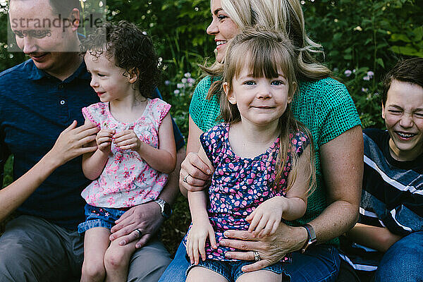 Mädchen sitzt auf dem Schoß der Mutter mit einer glücklich lächelnden Familie draußen