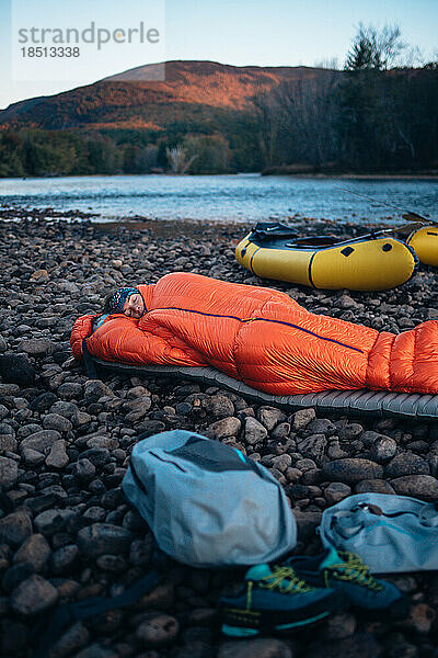 Frau schläft im Schlafsack am Flussufer mit Packflößen