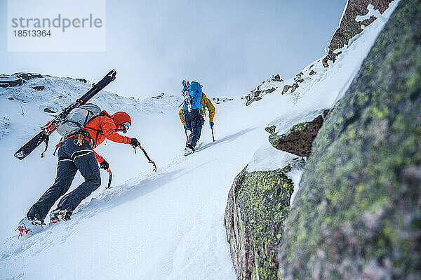 Zwei Männer erklimmen mit Skiern eine steile Schneerinne