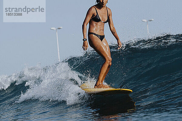 Unterer Teil einer Surferin im Bikini  die auf einem gelben Longboard surft