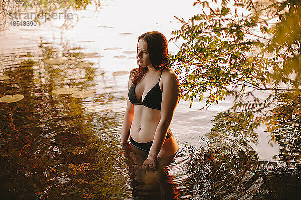 Junge Frau im Bikini steht bei Sonnenuntergang im Wasser