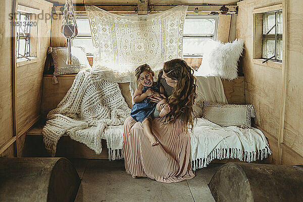 Mother and daughter cuddling and laughing in boho studio setup