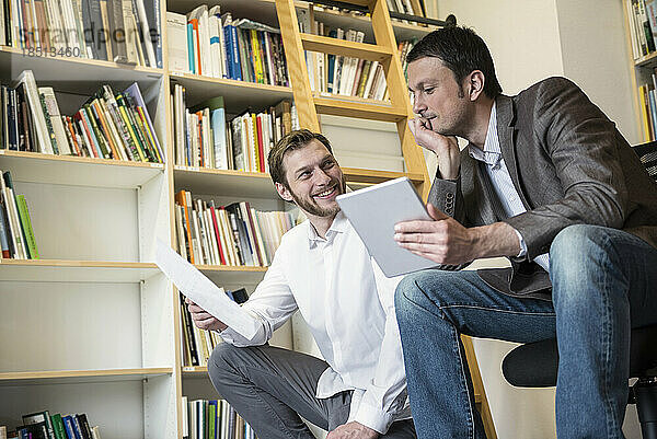 Zwei Geschäftsleute betrachten Notizen und nutzen ein digitales Tablet in einem Büro  Bayern  Deutschland