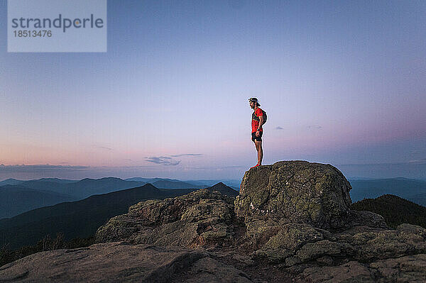 Trailrunner-Mann steht bei Sonnenaufgang auf einem Felsen auf dem Gipfel des Berges