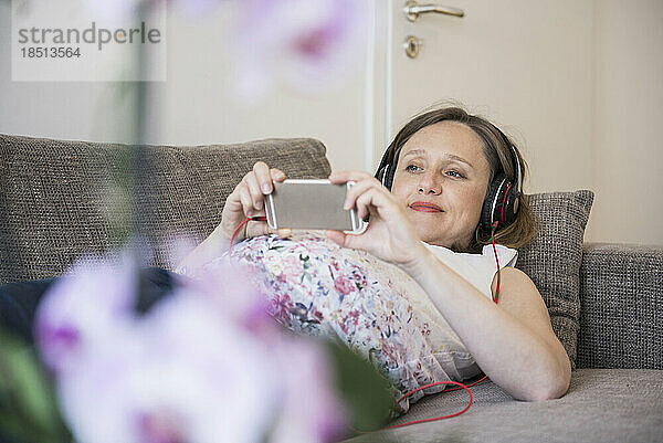 Schwangere Frau liegt auf Sofa und hört Musik  München  Bayern  Deutschland