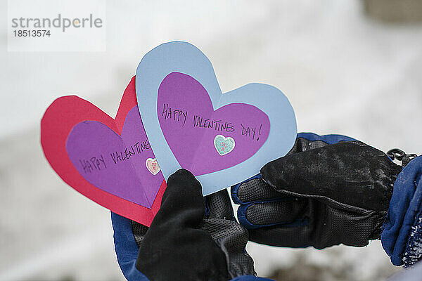 Nahaufnahme eines Kindes draußen im Winter  das Valentinstagskarten hält