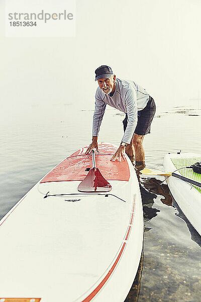 Reifer Mann schiebt sein Standup-Paddle-Board im Nebel ans Ufer