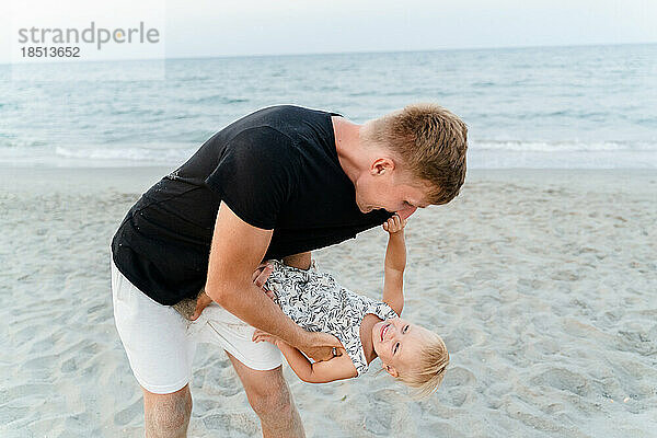 Ein Mann dreht sein kleines Mädchen an einem Sandstrand in seinen Armen