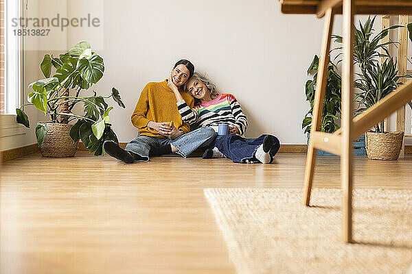 Lächelnde Mutter und Tochter sitzen zu Hause auf dem Hartholzboden