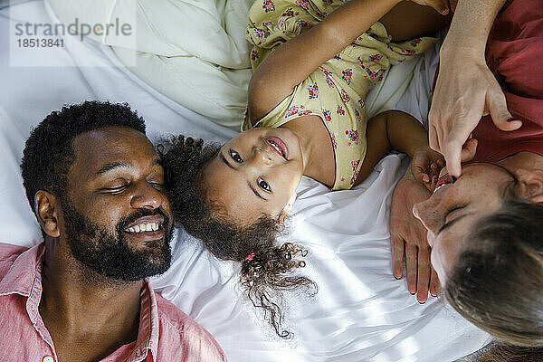Happy daughter lying down with parents on bed at home