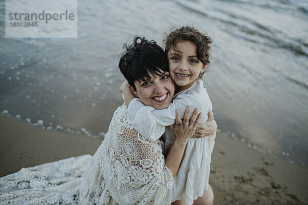 Glückliches Mädchen umarmt Mutter am Strand