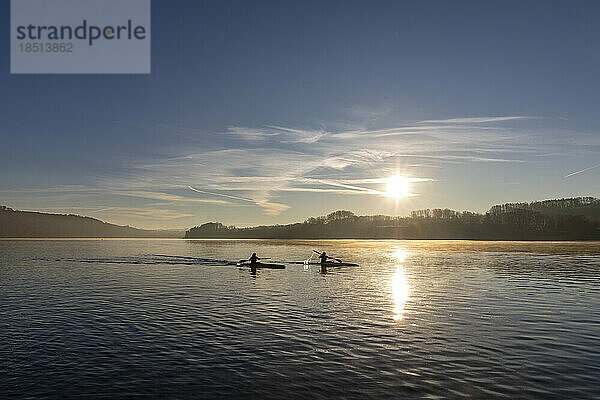 Silhouette of canoeists paddling in lake at sunrise