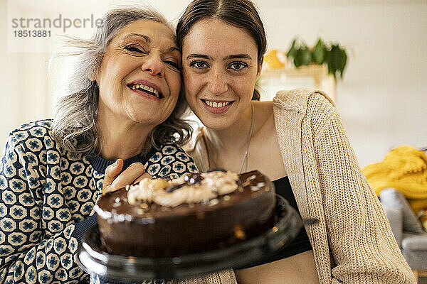 Glückliche Tochter mit Mutter  die zu Hause Kuchen hält