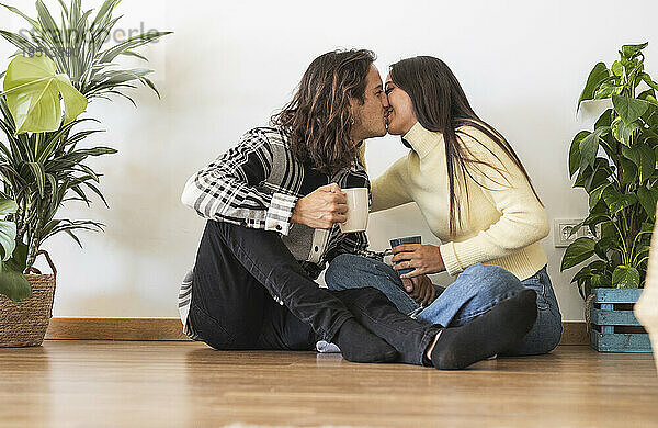 Romantisches Paar hält Kaffeetassen und küsst sich im neuen Zuhause