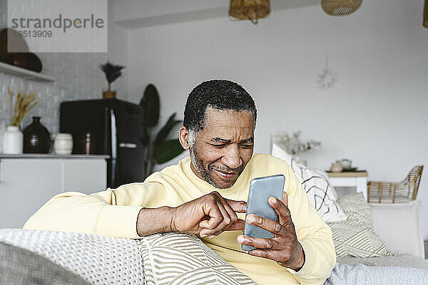 Lächelnder reifer Mann  der zu Hause sein Smartphone benutzt