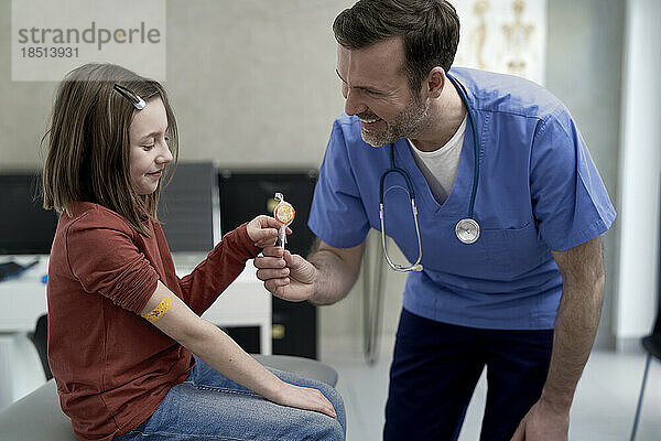 Happy mature doctor giving lollipop to girl in clinic