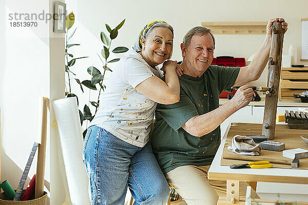 Glückliche ältere Frau mit der Hand auf der Schulter auf Mann  der in der Werkstatt Lack auf Holz aufträgt