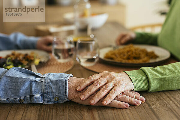 Senior woman stacking hand on man at dining table