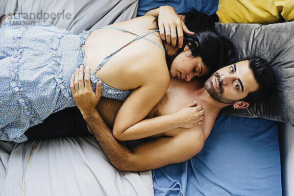 Shirtless man lying on bed with girlfriend at home
