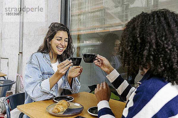 Fröhliche junge Freunde stoßen auf eine Kaffeetasse an und genießen sie im Straßencafé