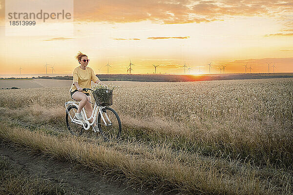 Frau fährt bei Sonnenuntergang Fahrrad auf dem Feld