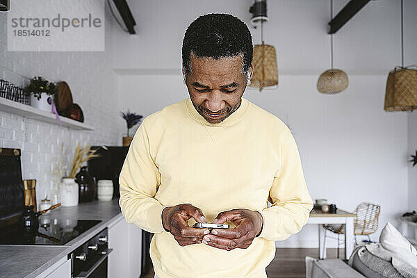 Reifer Mann benutzt Smartphone in der heimischen Küche