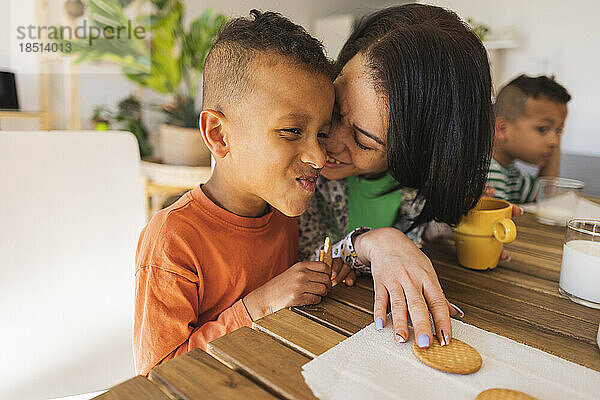 Affectionate mother embracing son having breakfast at home