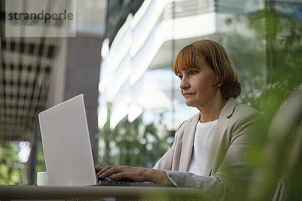 Konzentrierte Geschäftsfrau arbeitet am Laptop im Straßencafé