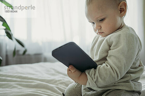 Kleinkind hält Smartphone zu Hause im Bett