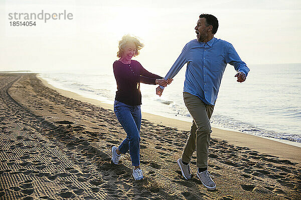 Cheerful mature woman running with man at coastline