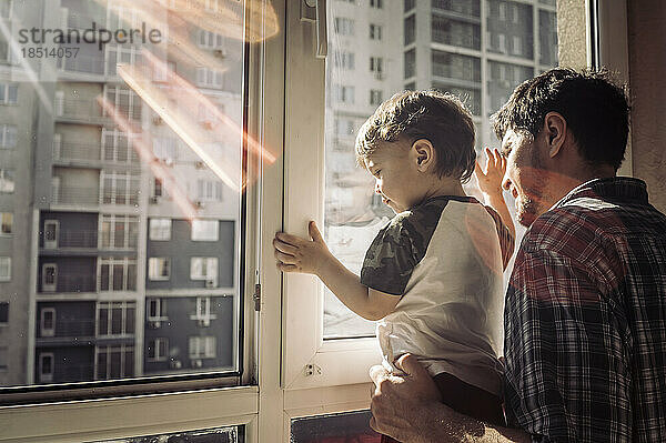 Vater und Sohn schauen zu Hause aus dem Fenster