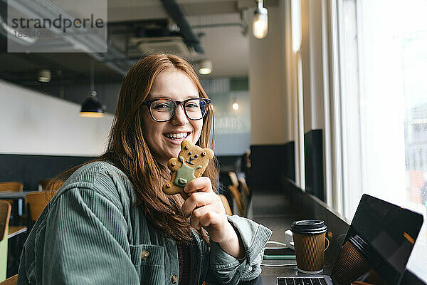 Glücklicher junger Freiberufler mit Teddybär-Keks im Café