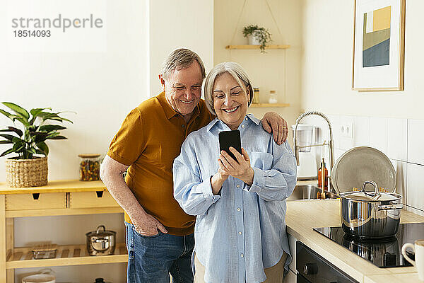 Glückliche Seniorin teilt Smartphone mit Mann in der Küche