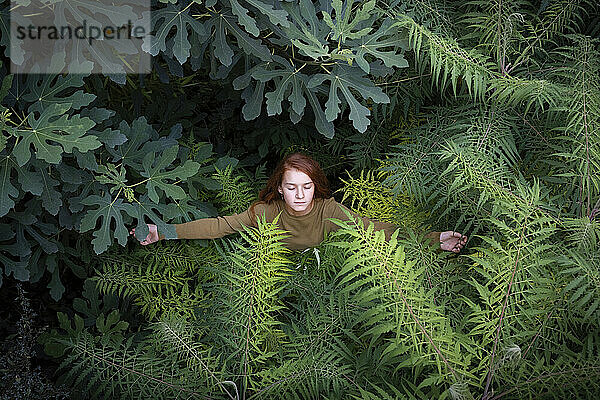 Mädchen mit geschlossenen Augen steht inmitten von Pflanzen
