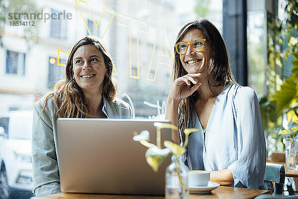 Lächelnde Geschäftsfrauen sitzen mit Laptop am Tisch im Café
